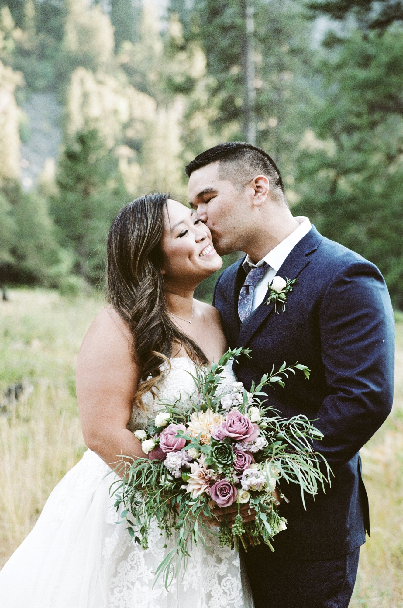 a groom kissing his bride with a bouquet of flowers